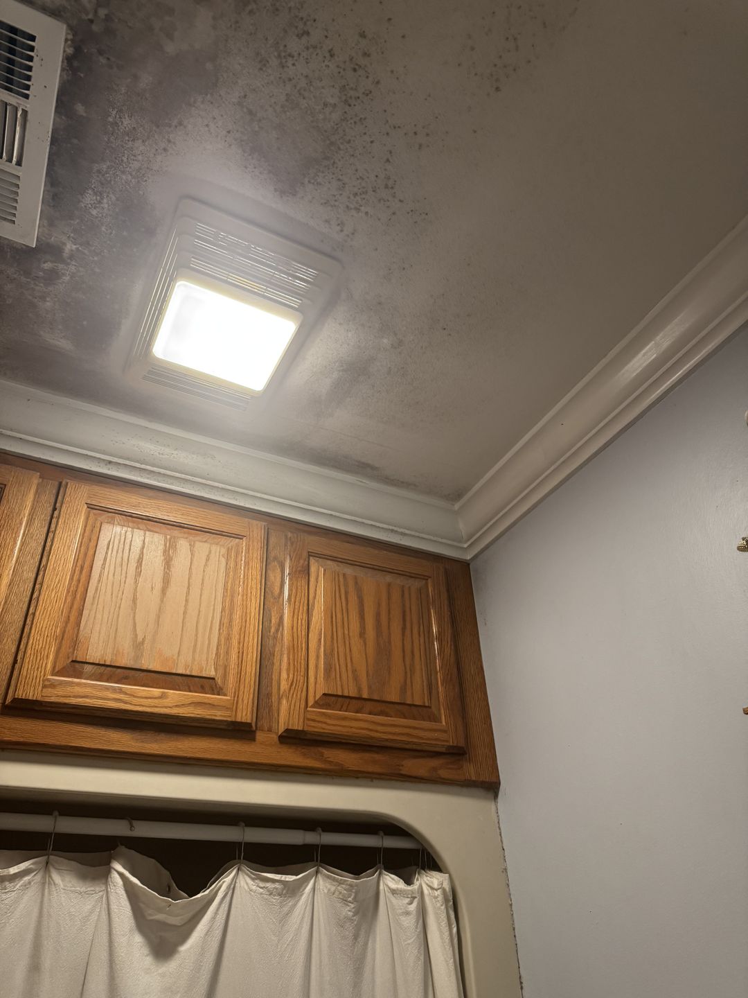 Growth clouding a bathroom ceiling above the cabinets and exhaust fan